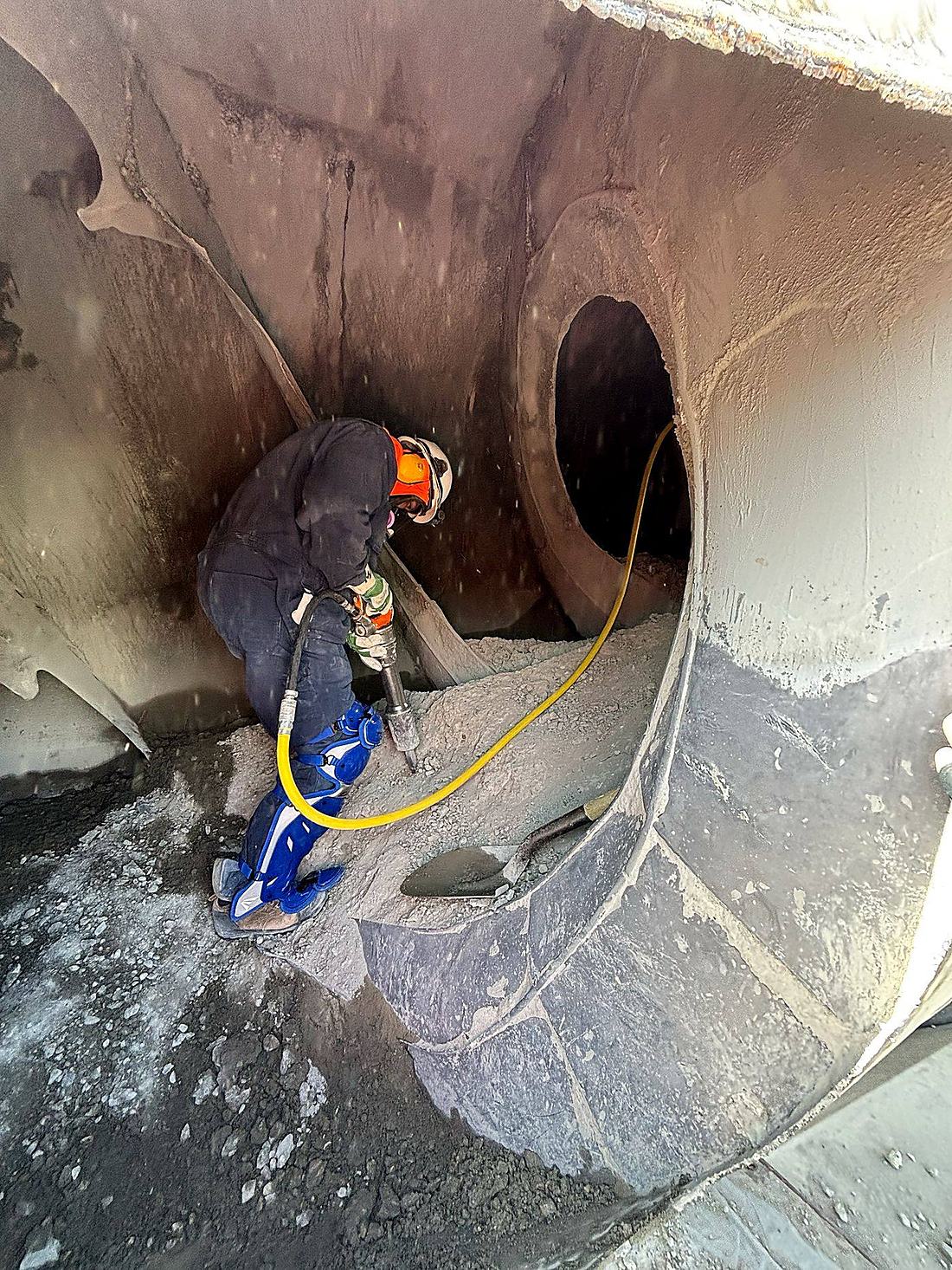 Chipping technician removing hardened concrete buildup from the fins inside a ready mix drum with a pneumatic hammer